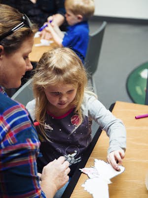 A child and mother create create a butterfly out of paper