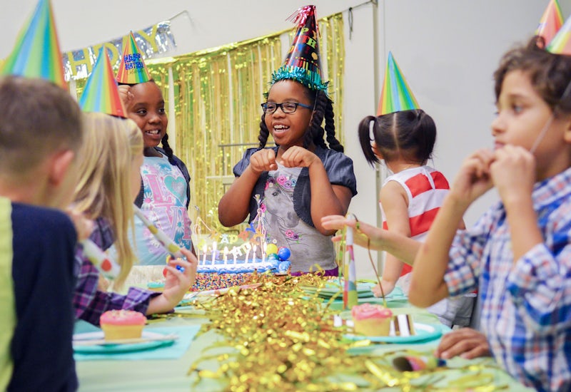 Laughing girl in party hat, celebrating her birthday with friends.